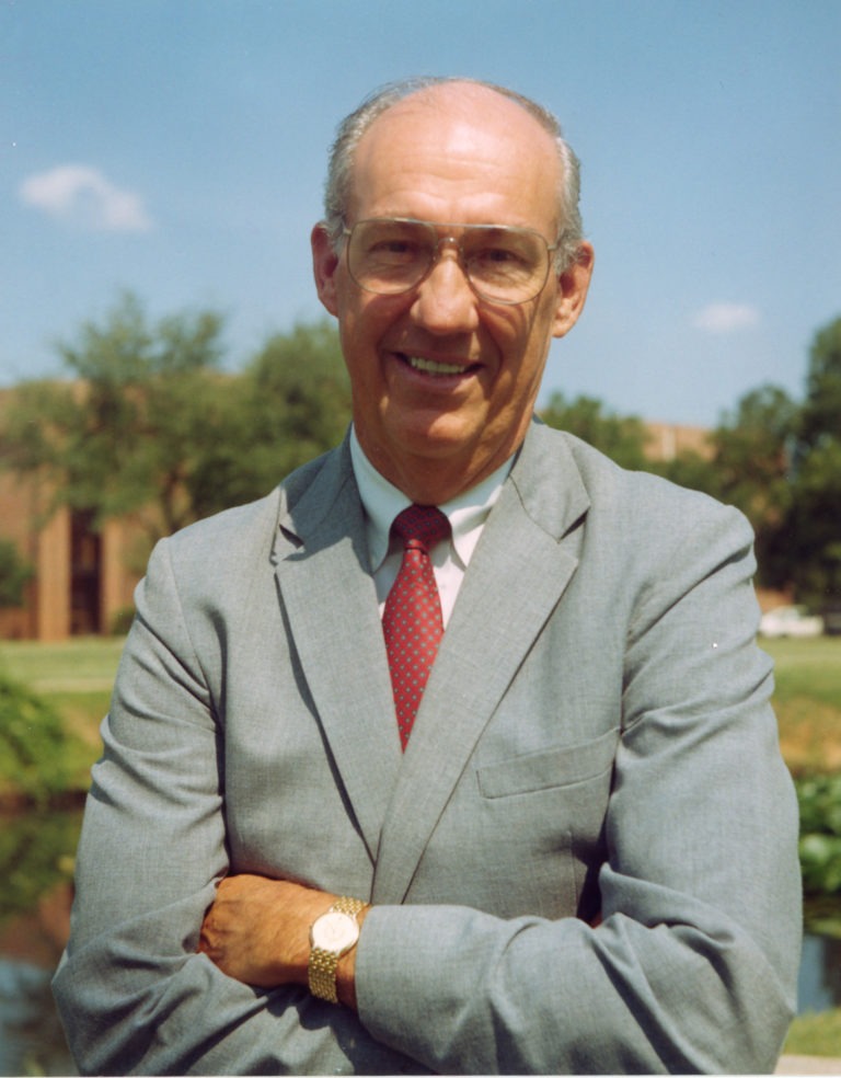 Jesse C. Fletcher smiling in a suit with arms crossed