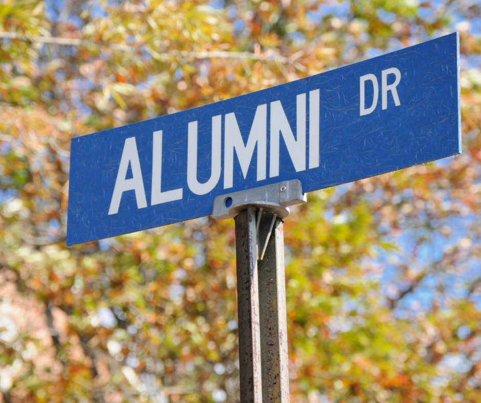 Picture of a blue street sign that says Alumni Drive, with fall leaves in the background