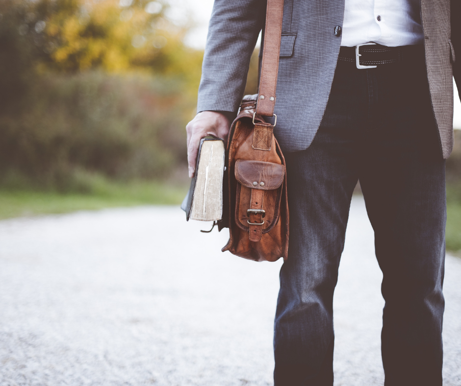 Picture of a male wearing a sport-coat and jeans, with a brown messenger bag over his shoulder and also a textbook in hand