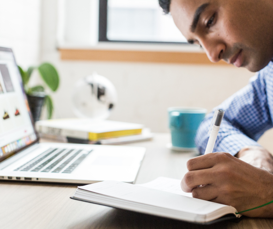 Hispanic student studying online and writing in a notebook