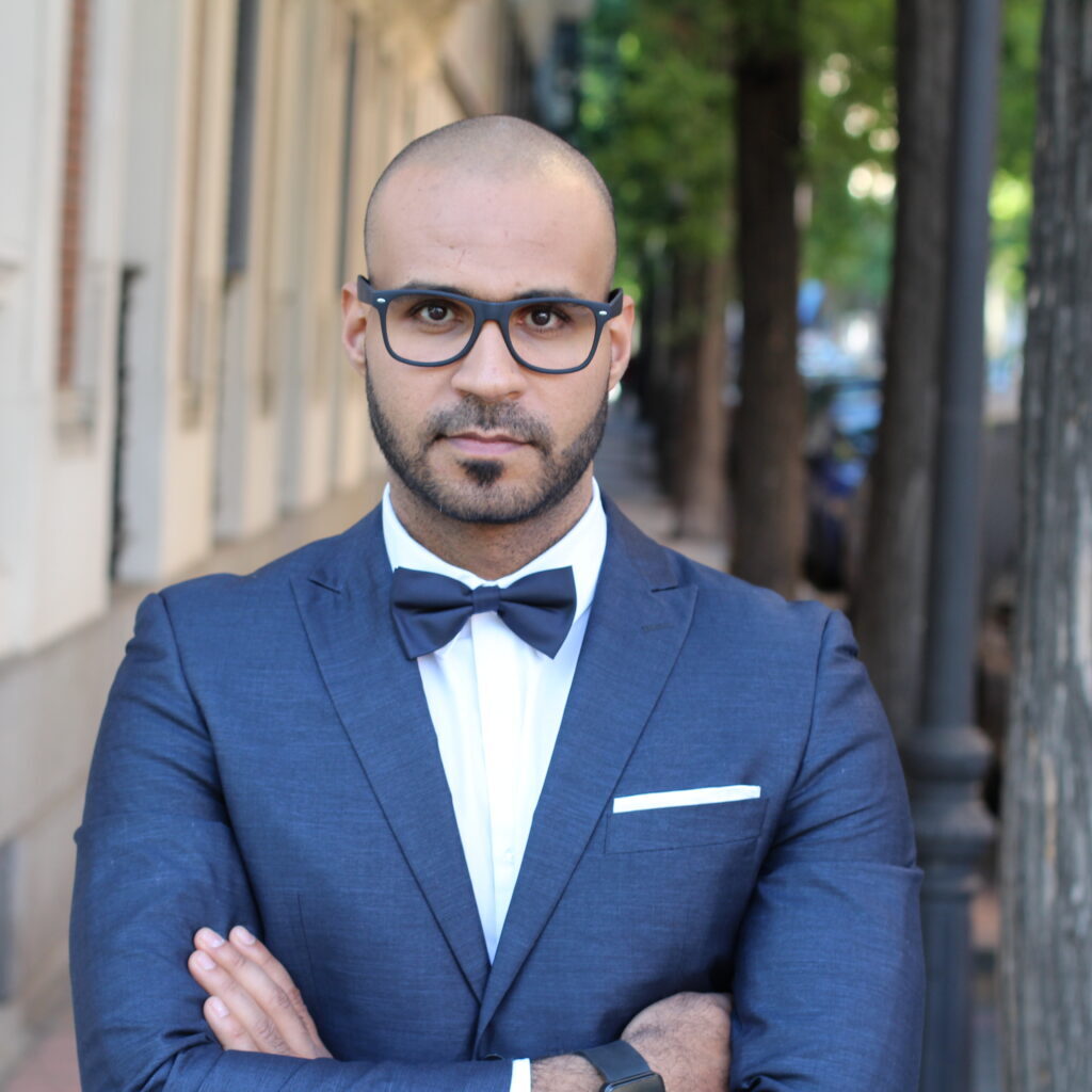 A man stands with his arms crossed in a suit